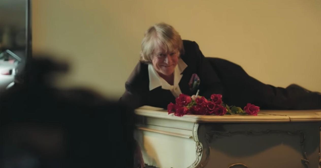 Mann im Anzug liegt auf einem Möbelstück mit roten Rosen.