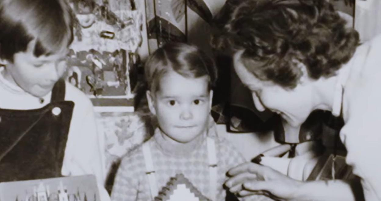 Zwei Kinder und eine Frau blicken auf ein Buch, das ein Kind hält.
