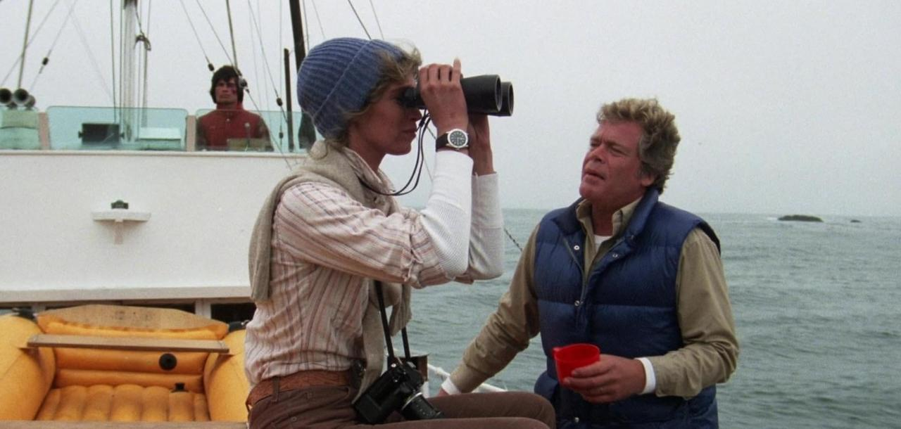 Frau blickt durch Fernglas, Mann hält rote Tasse. Auf einem Boot.