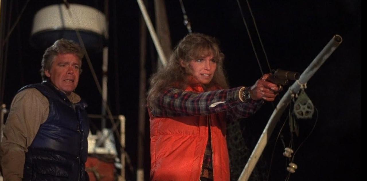 Mann mit Weste und Frau mit Waffe auf einem Boot bei Nacht.