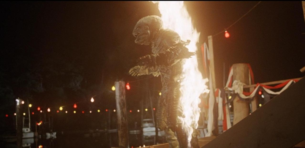 Ein Wesen in Flammen steht nachts unter Lichterketten.