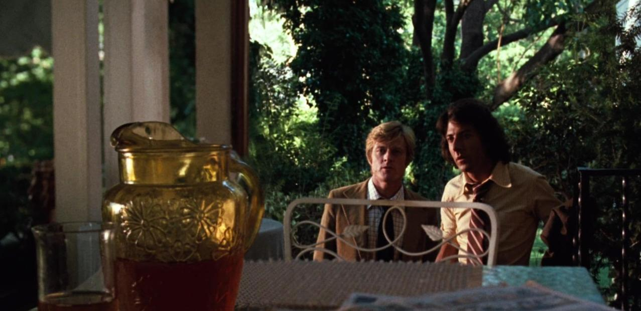 Zwei Männer sitzen im Freien bei einem Tisch mit einer goldenen Karaffe und Saft.