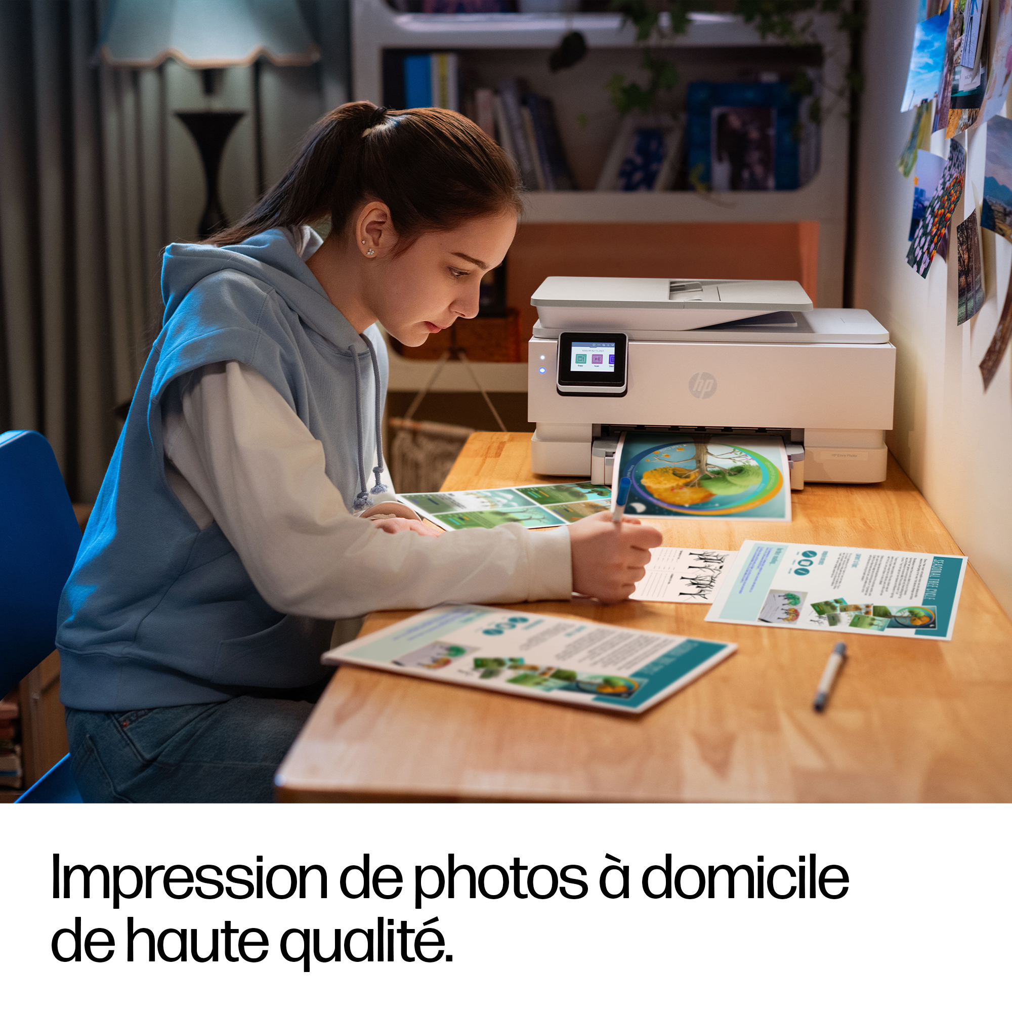 Une fille imprime des photos sur une imprimante HP. Des papiers sont sur la table.