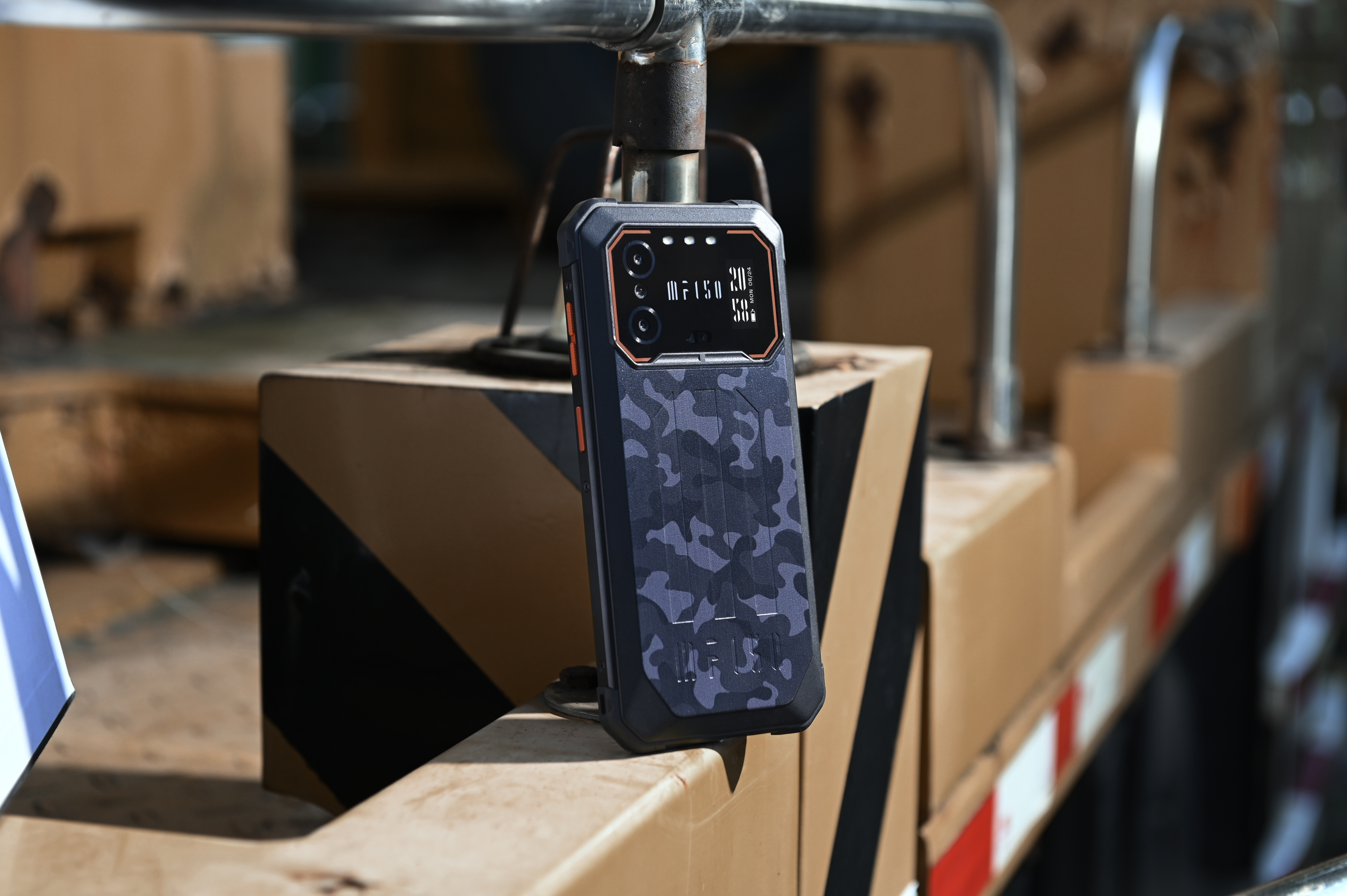 Wytrzymały smartfon z motywem kamuflażu spoczywa na drewnianej skrzyni.