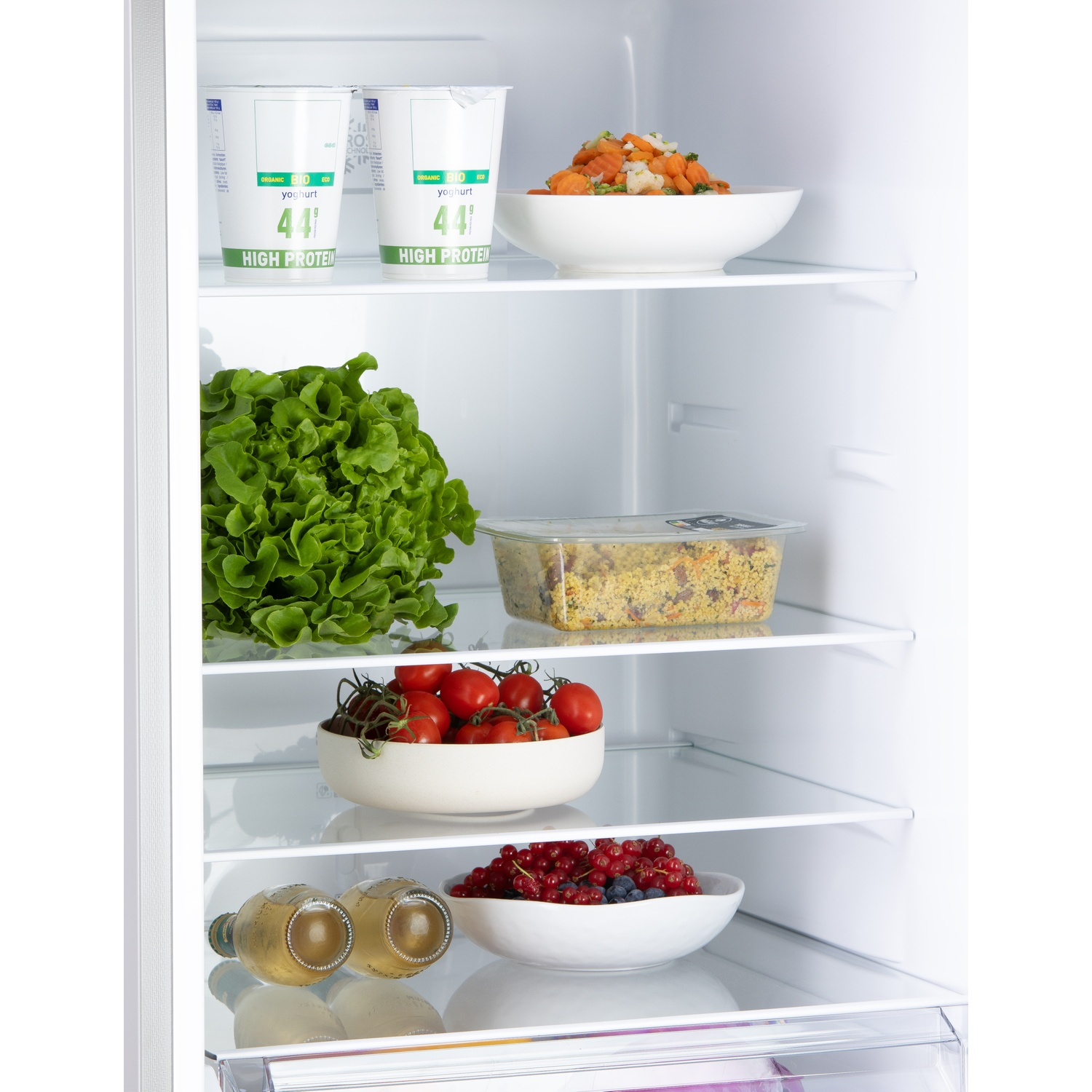 Un réfrigérateur ouvert avec yaourt, légumes, tomates, baies et bouteilles.