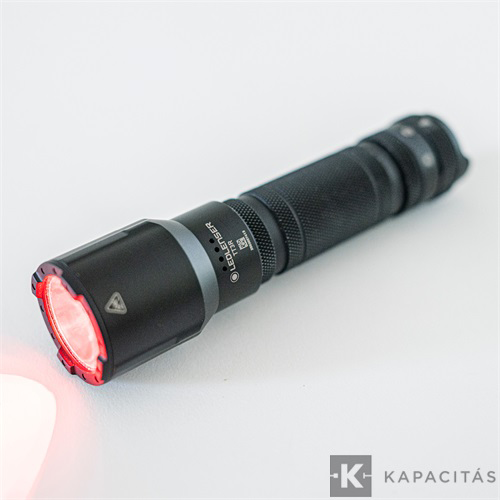 Fekete LED zseblámpa piros fénnyel a fején, fehér háttéren.