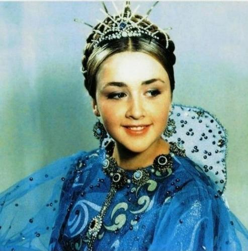 Eine junge Frau trägt eine blaue, verzierte Kleidung und einen funkelnden Diadem.