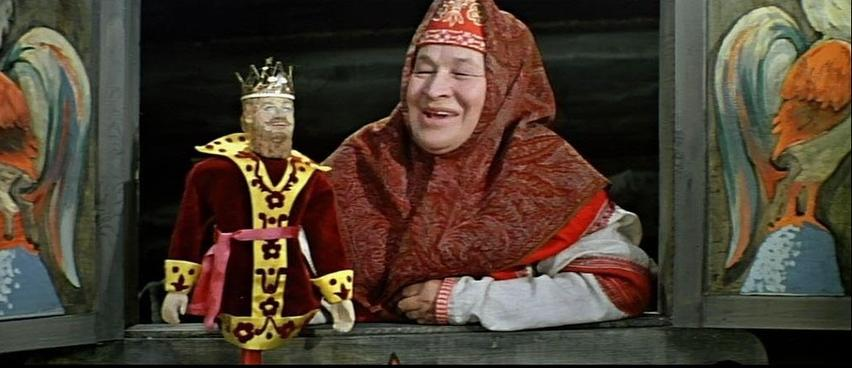 Eine Frau in traditioneller Kleidung neben einer Marionette eines Königs.