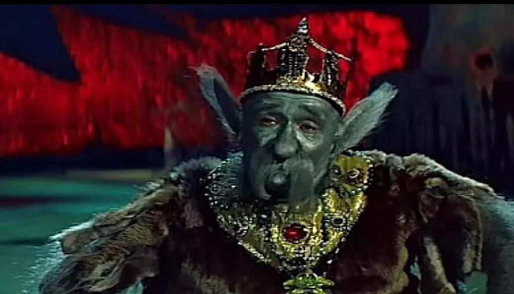 Ein grüner König mit Krone und Pelzmantel trägt Schmuck.