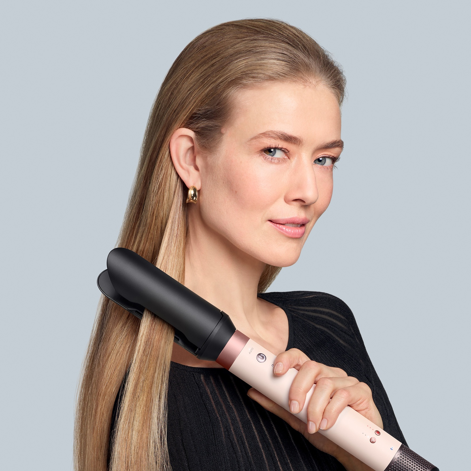 Woman with long blonde hair holds a pink hair styler.