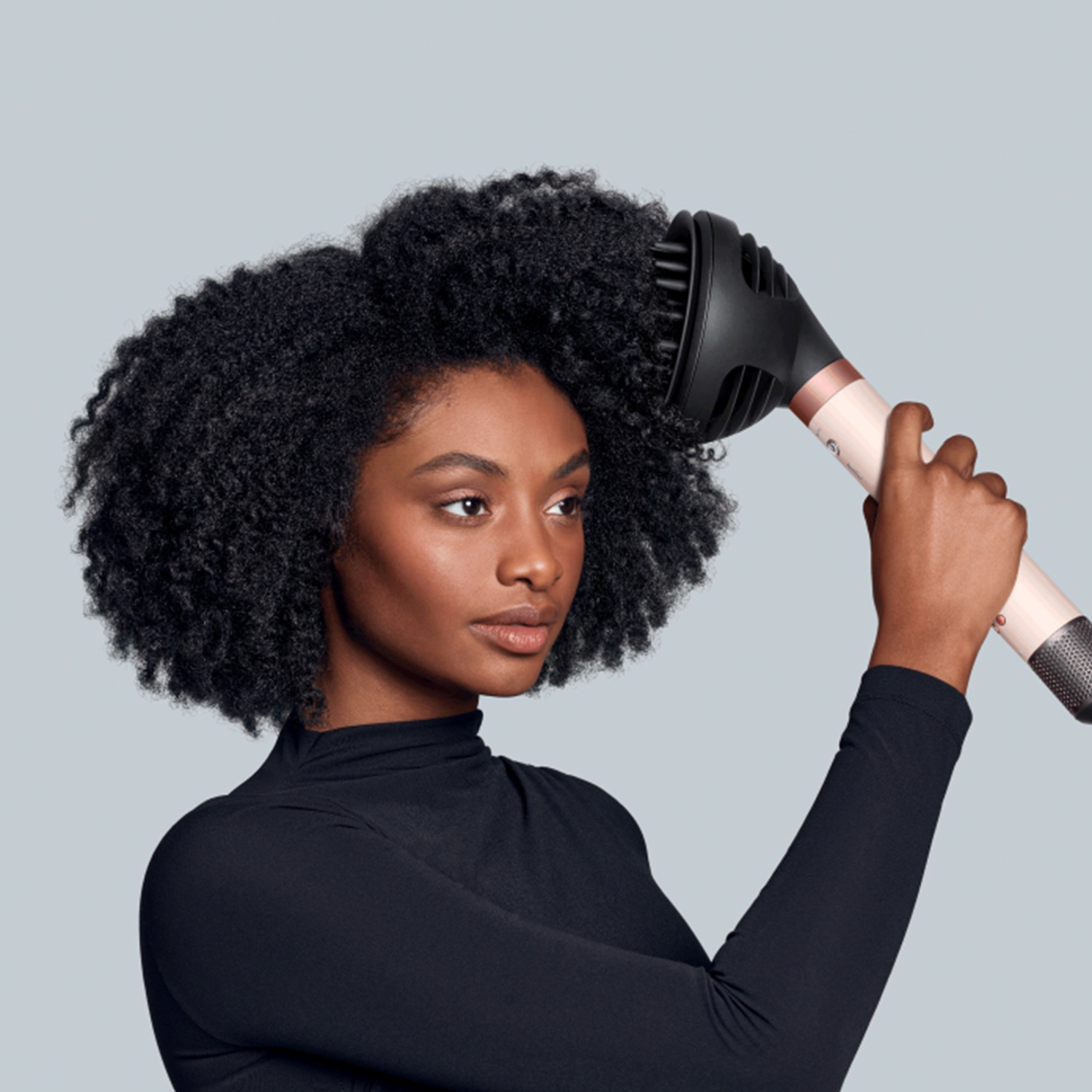 Woman with afro hair using a diffuser attachment on a hairdryer.