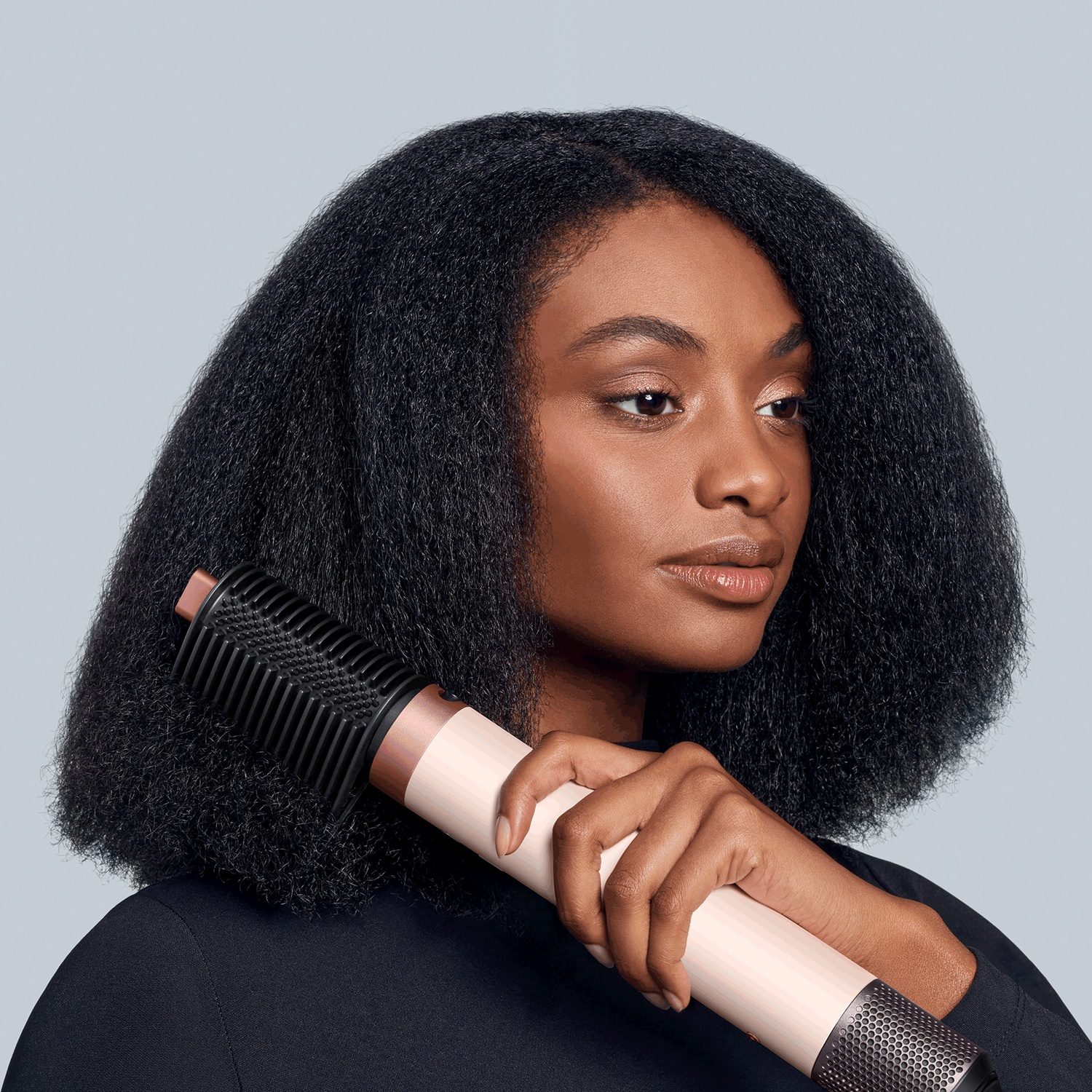 A woman with dark hair holds a rose gold accented hair styling tool.