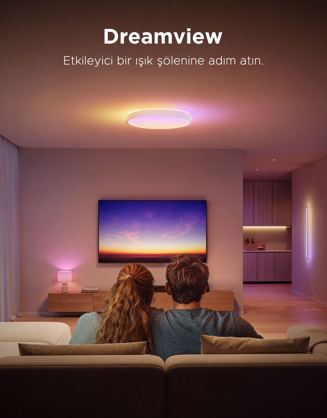 Bir çift koltukta oturmuş TV izliyor. Tavan lambası renkli tonlar yansıtıyor.