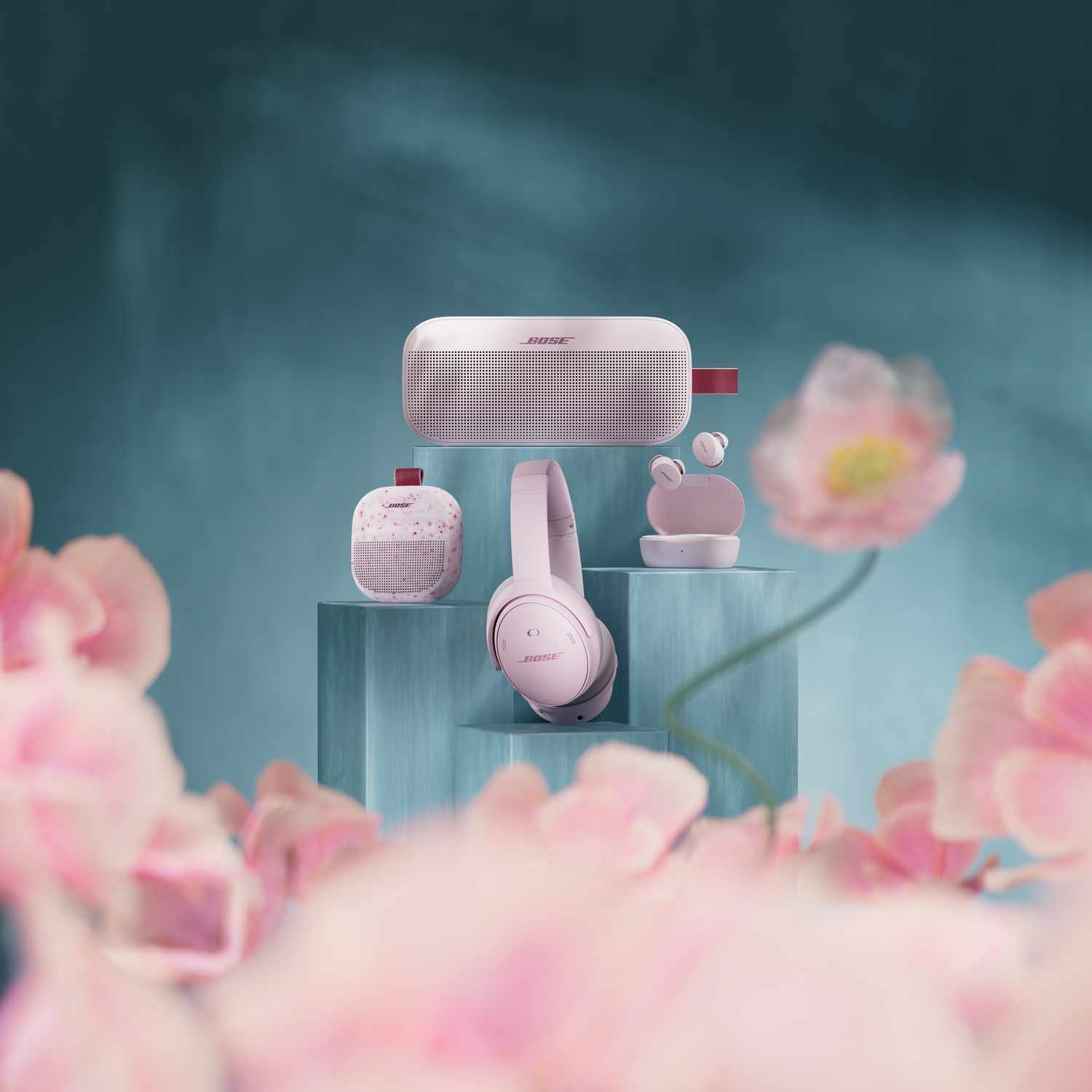 Cuffie, altoparlanti e auricolari Bose rosa su piedistalli blu con fiori in primo piano.