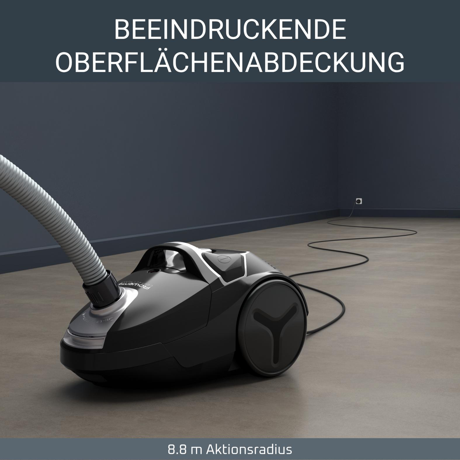 Schwarzer Staubsauger mit Schlauch auf grauem Boden, Kabel in Steckdose.