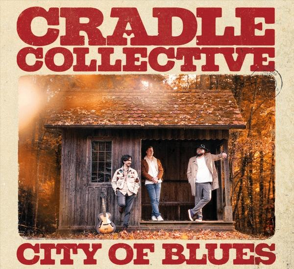 Drei Männer stehen vor einer Holzhütte im Herbst. Titel: CRADLE COLLECTIVE CITY OF BLUES.