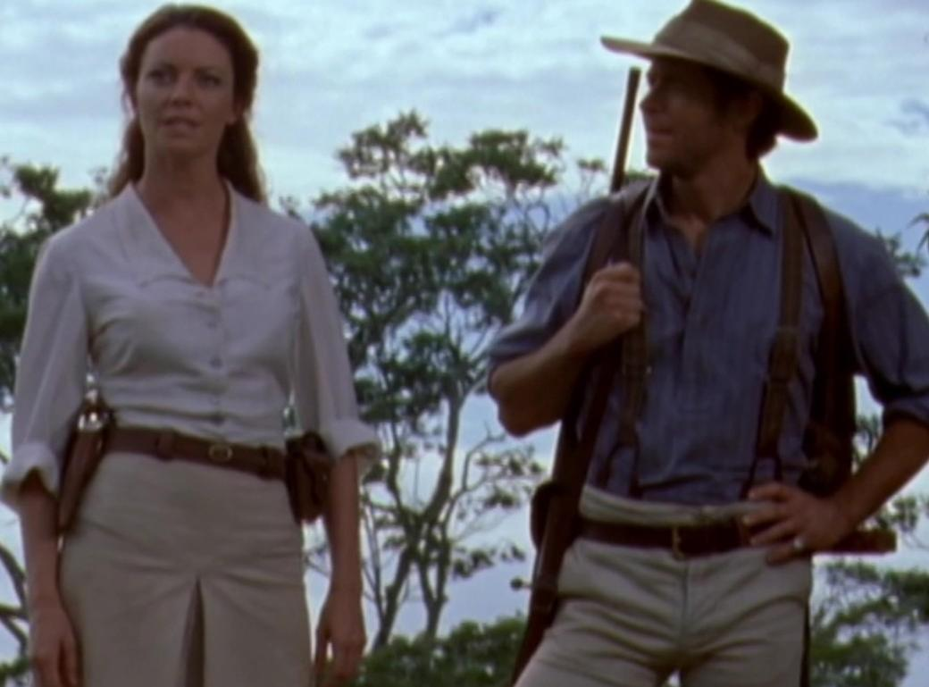 Ein Mann und eine Frau im Freien, beide im Abenteurer-Outfit, Bäume im Hintergrund.