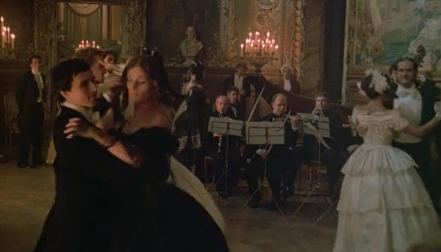 Ein Ballsaal mit tanzenden Paaren und einem Orchester im Hintergrund.