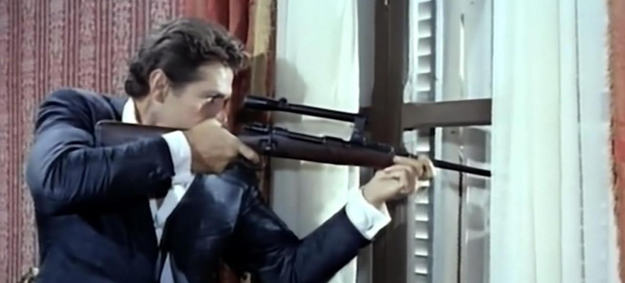 Ein Mann im Anzug zielt mit einem Gewehr durch ein Fenster.