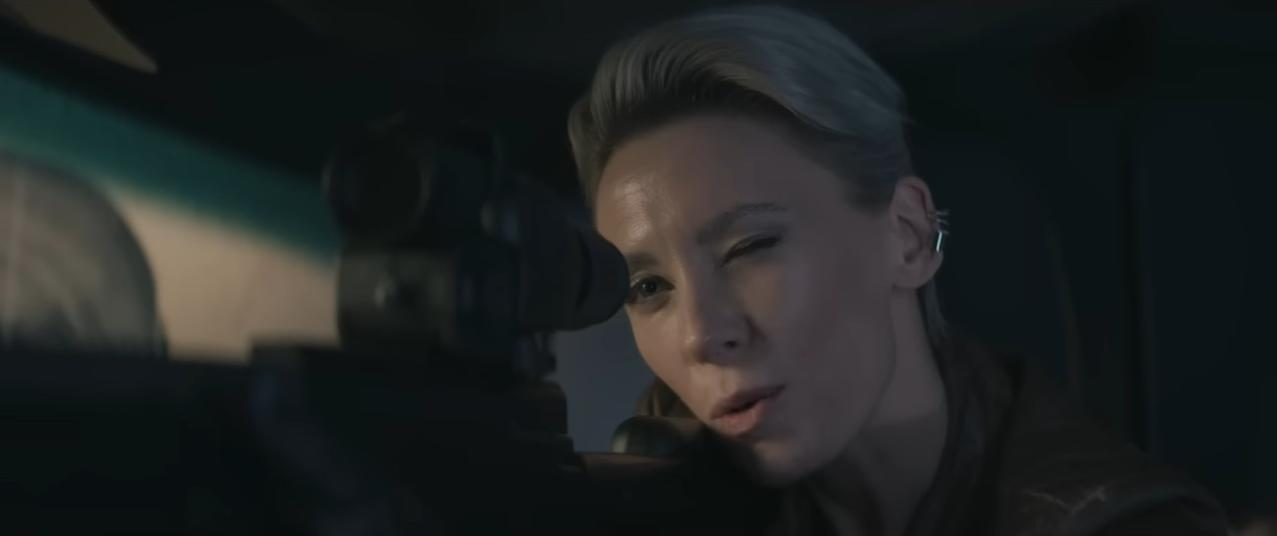 Eine Frau mit kurzen grauen Haaren zielt mit einem Gewehr, ein Auge geschlossen.