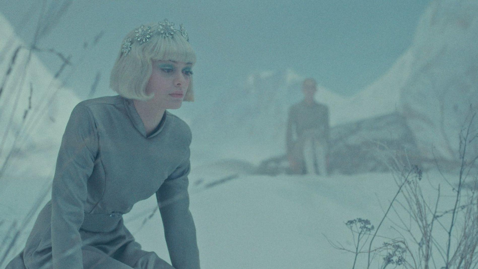 Eine Frau mit silbernem Kopfschmuck in einem grauen Kleid kniet in einer verschneiten Landschaft.