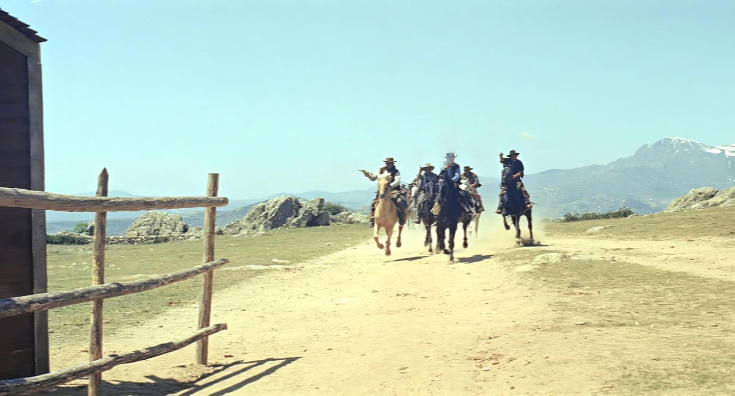 Cowboys auf Pferden reiten einen staubigen Pfad entlang mit Bergen im Hintergrund.