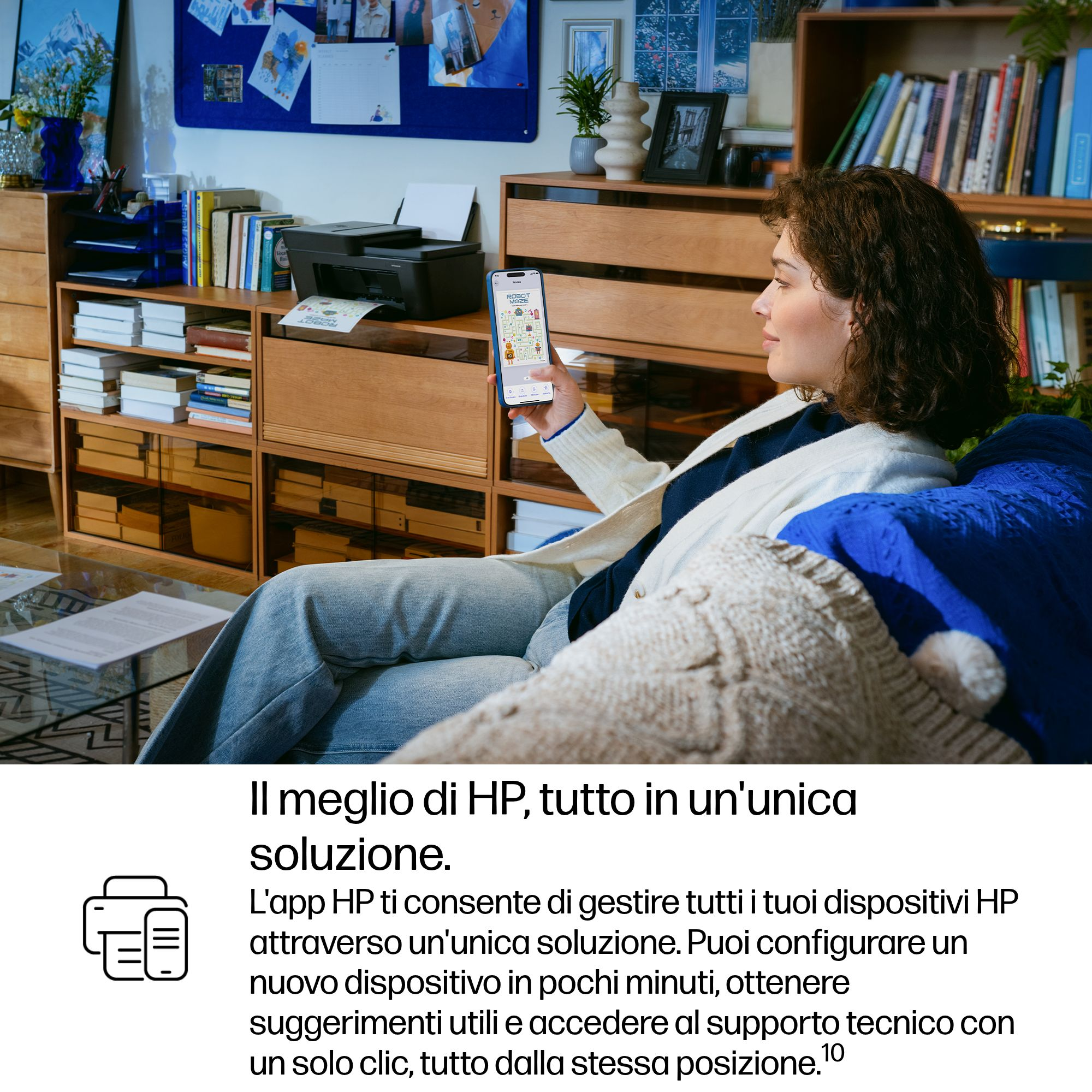Una donna seduta su un divano tiene uno smartphone con un'app, accanto a una stampante.
