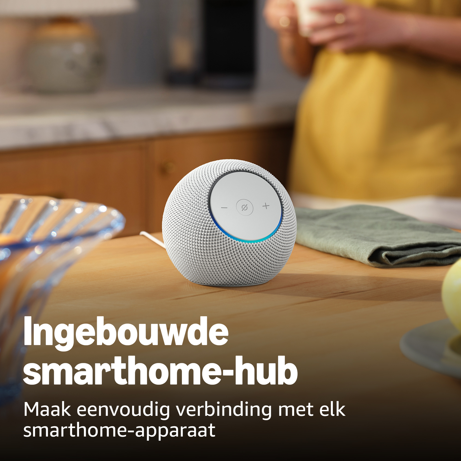 A white smart home speaker sits on a wooden table next to a bowl.