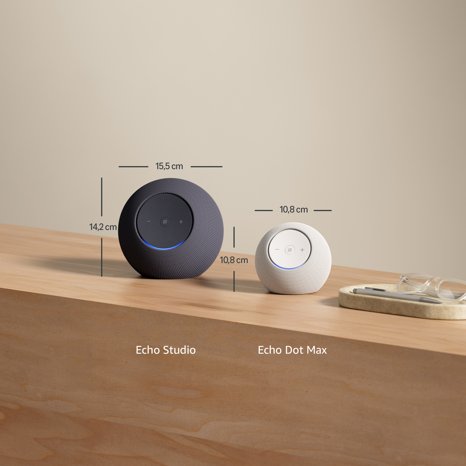 Two smart speakers on a wooden surface. Left is dark gray Echo Studio, right is white Echo Dot Max.