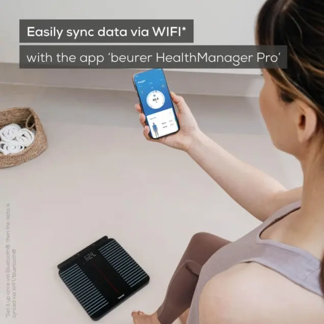 Une femme tient un smartphone au-dessus d'une balance numérique. Les données se synchronisent.