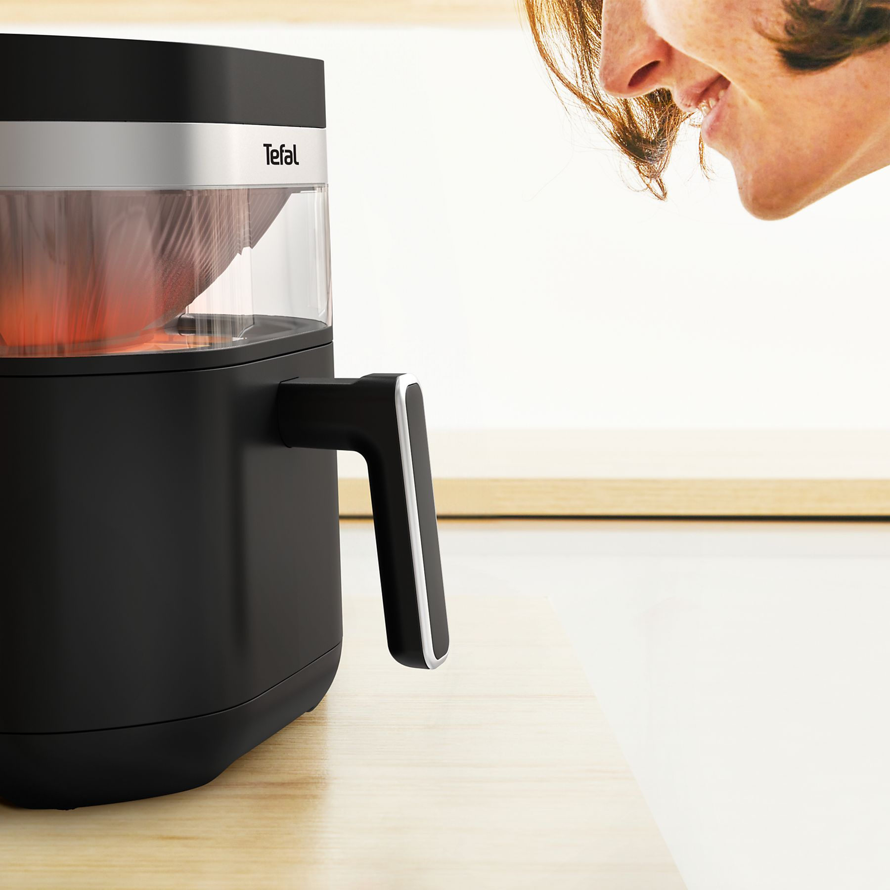 Une friteuse à air Tefal noire avec un récipient transparent montrant une lumière rouge à l'intérieur.
