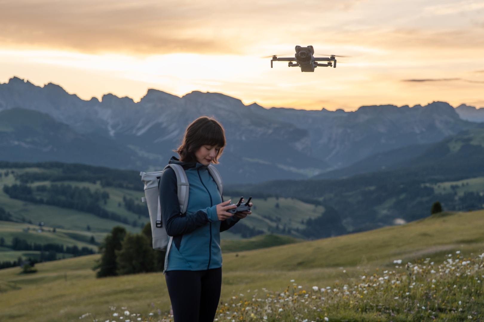 Donna controlla drone al tramonto con montagne sullo sfondo.
