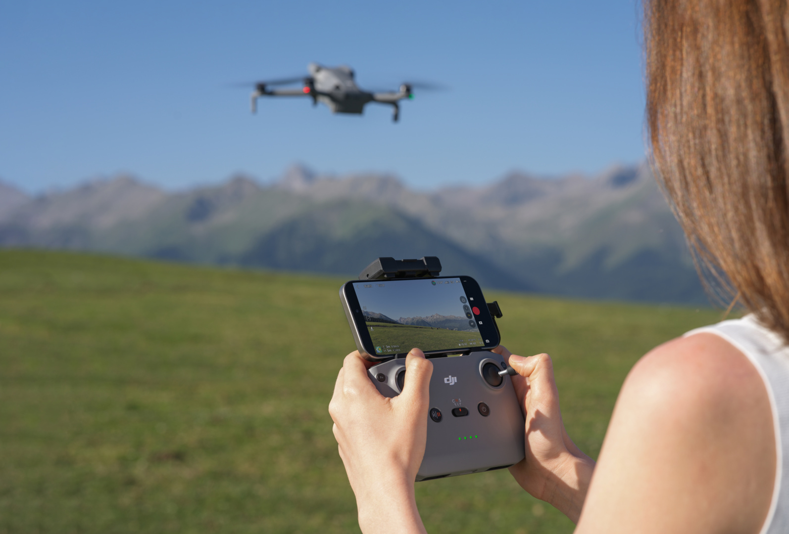 Drone che vola su campo verde, controllato da persona con telecomando.