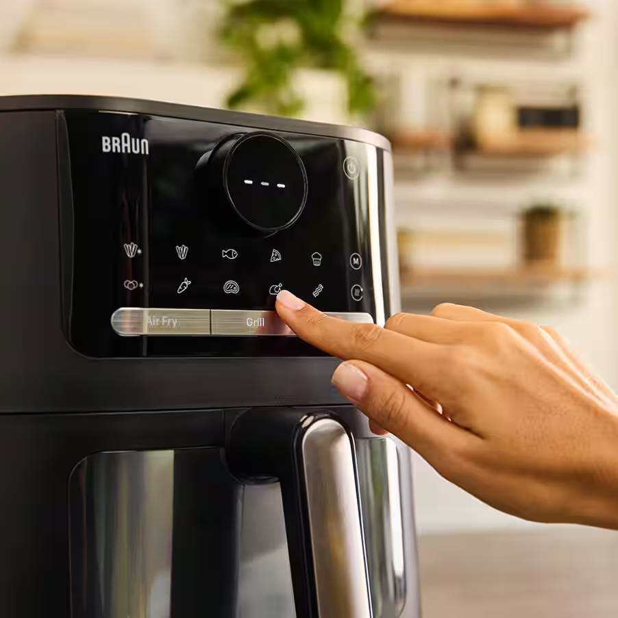 Une main appuie sur l'icône de grill d'une friteuse à air Braun. Des icônes de divers aliments sont visibles.