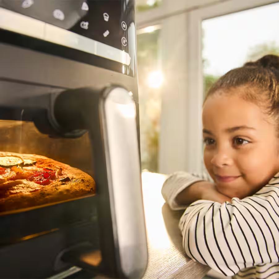 Une fille regarde une pizza cuire dans un four.