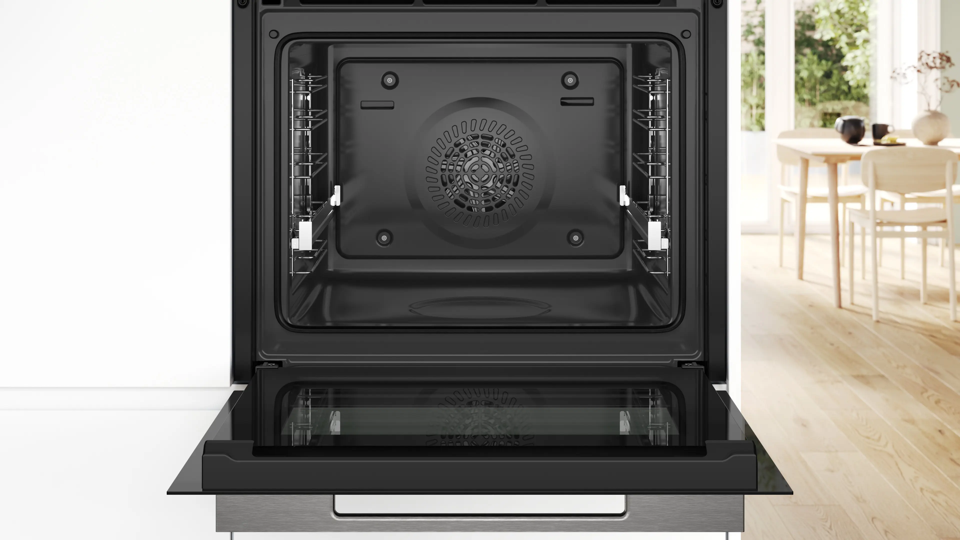 Un horno empotrado abierto con interior negro y rejilla. Una mesa de comedor al fondo.