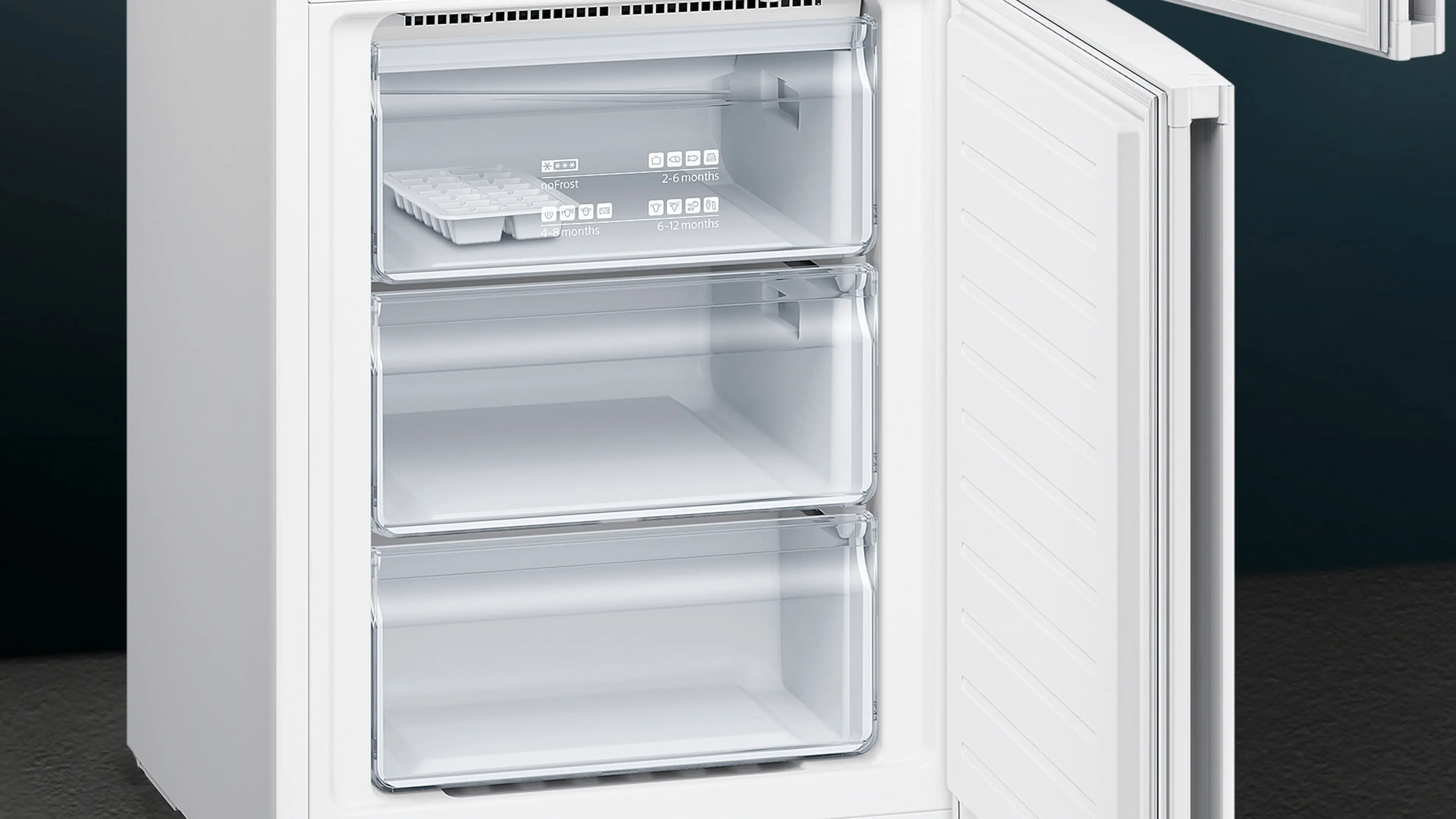 Congelador blanco abierto con tres cajones transparentes. El cajón superior tiene una cubitera.