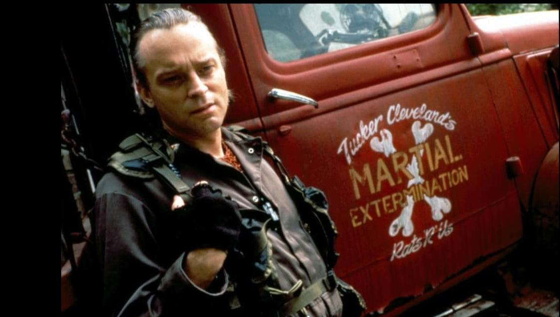 Ein Mann in Uniform steht vor einem roten LKW mit der Aufschrift 'Martial Extermination'.