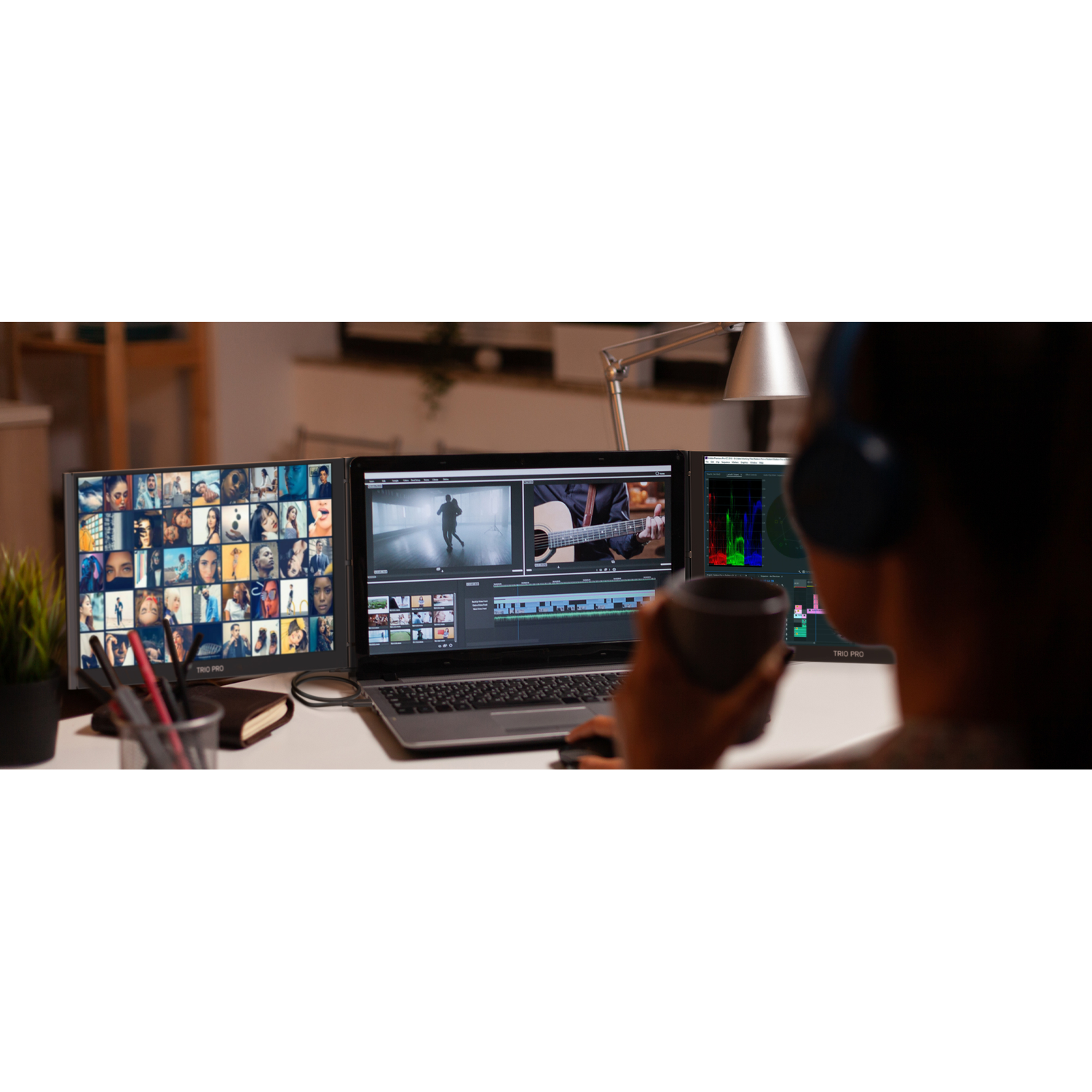 Person with headphones drinks from mug viewing three monitors: grid of faces, video editing, color grading.