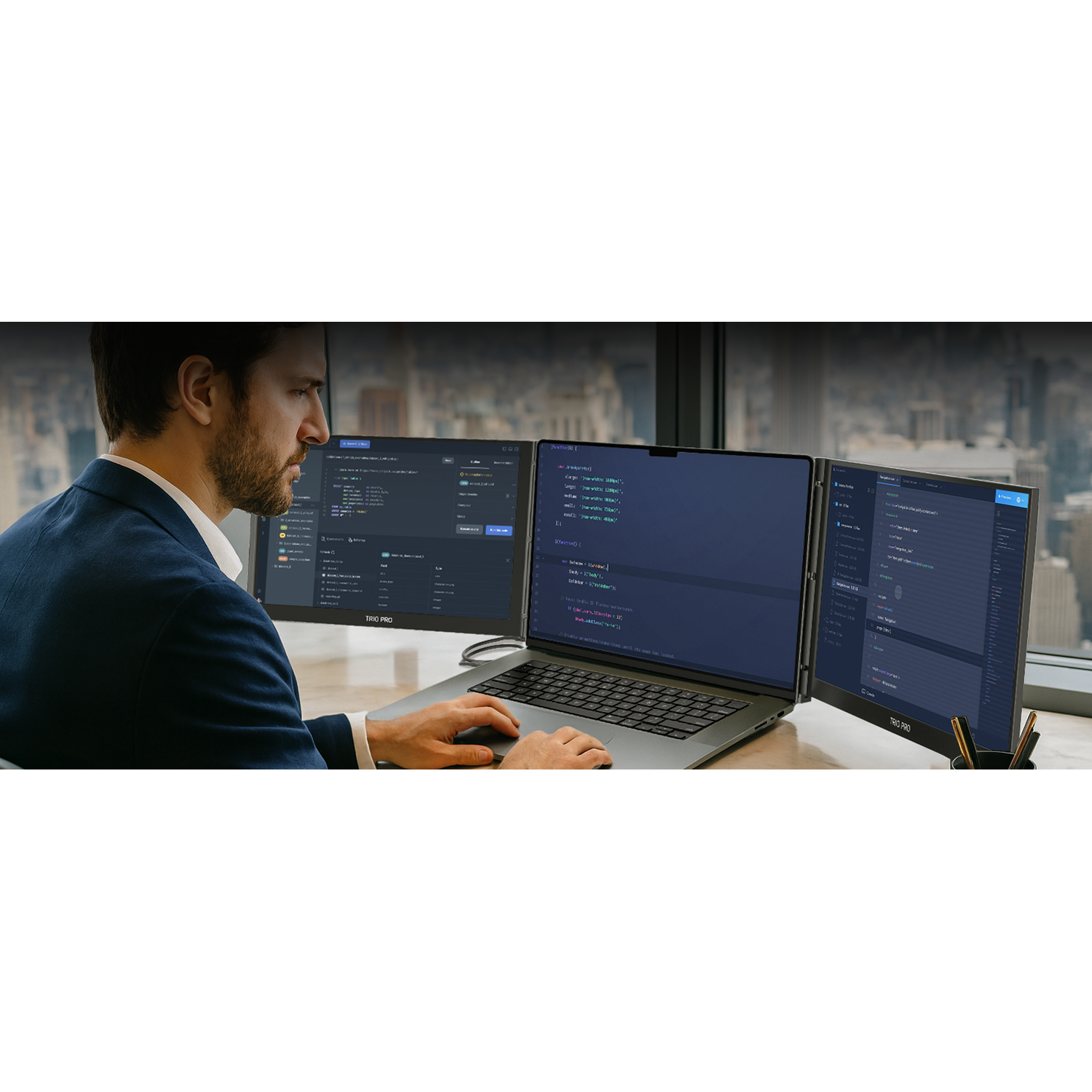 Man in a dark blue suit works on a laptop with three monitors.