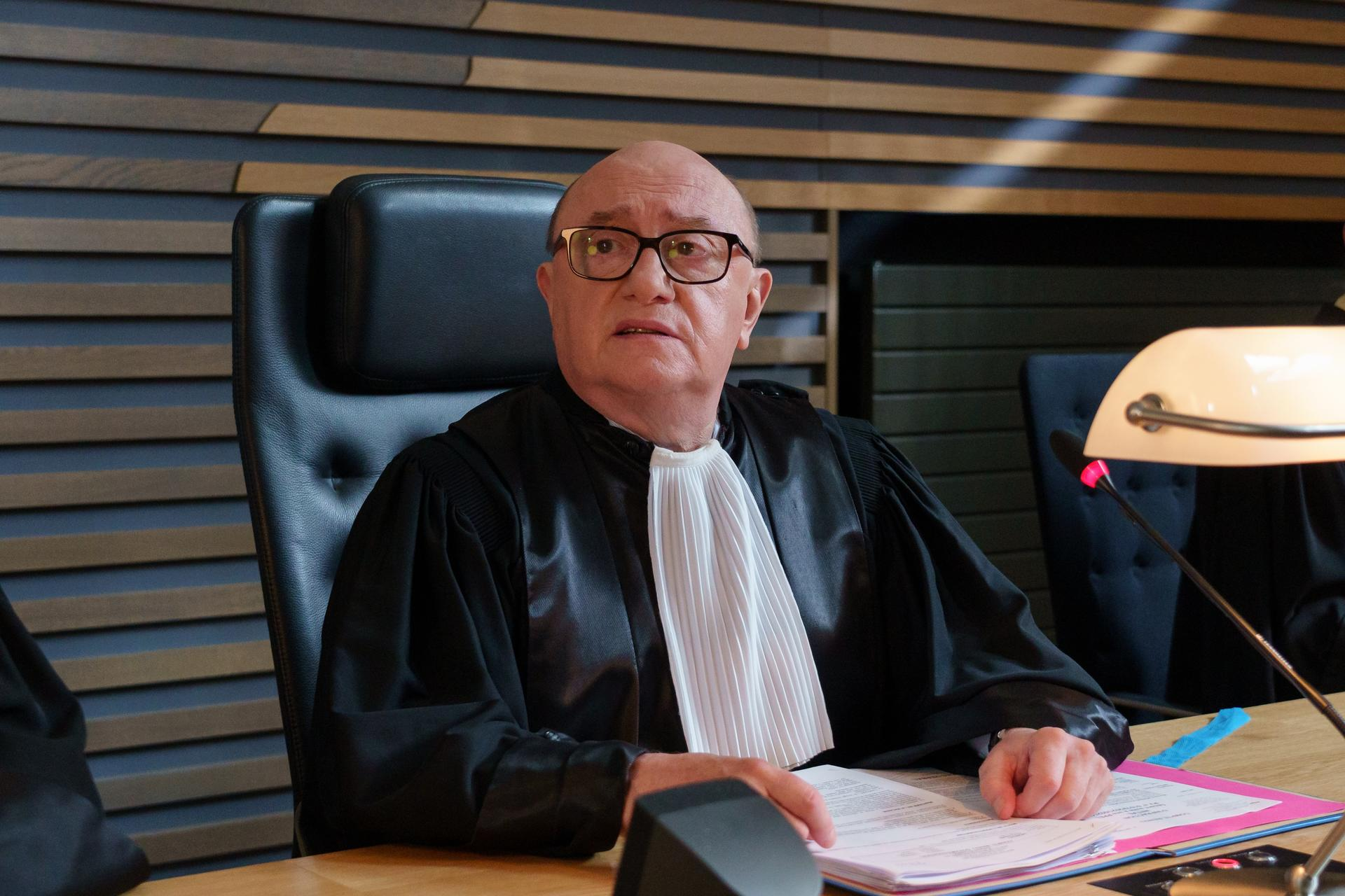 Ein kahler Mann mit Brille in Richterrobe sitzt am Tisch, Dokumente vor sich.
