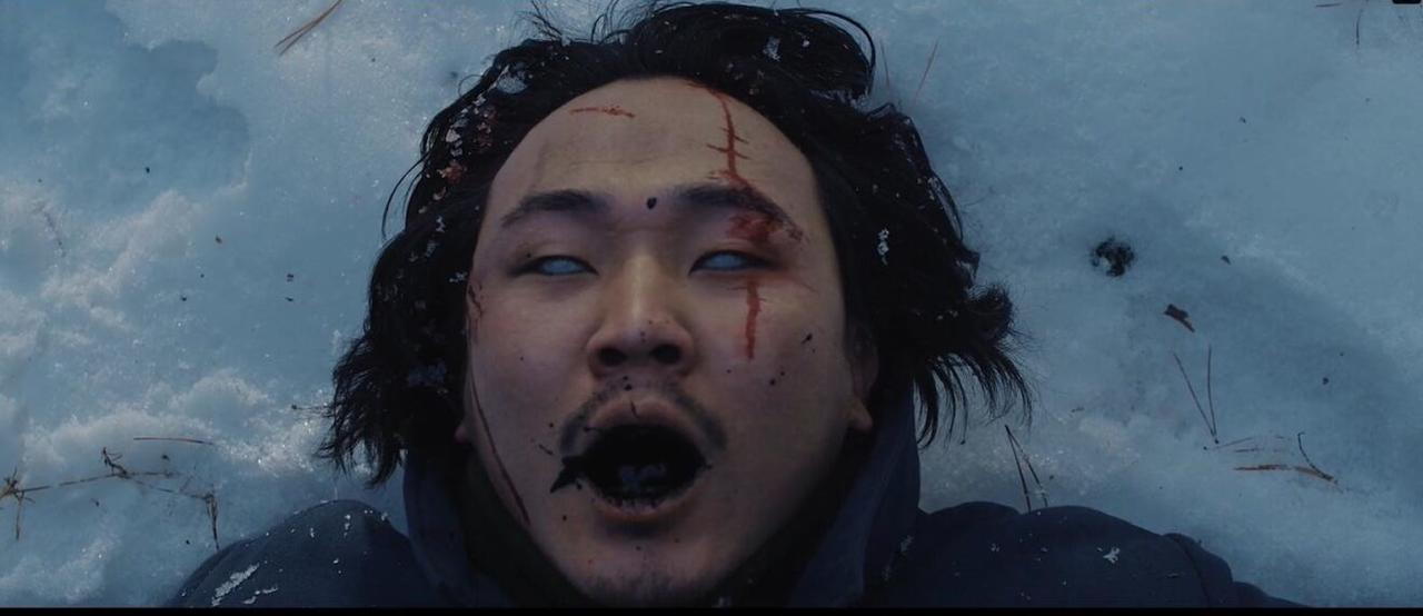 Ein Mann liegt im Schnee, sein Gesicht ist blutig, die Augen sind weiß.