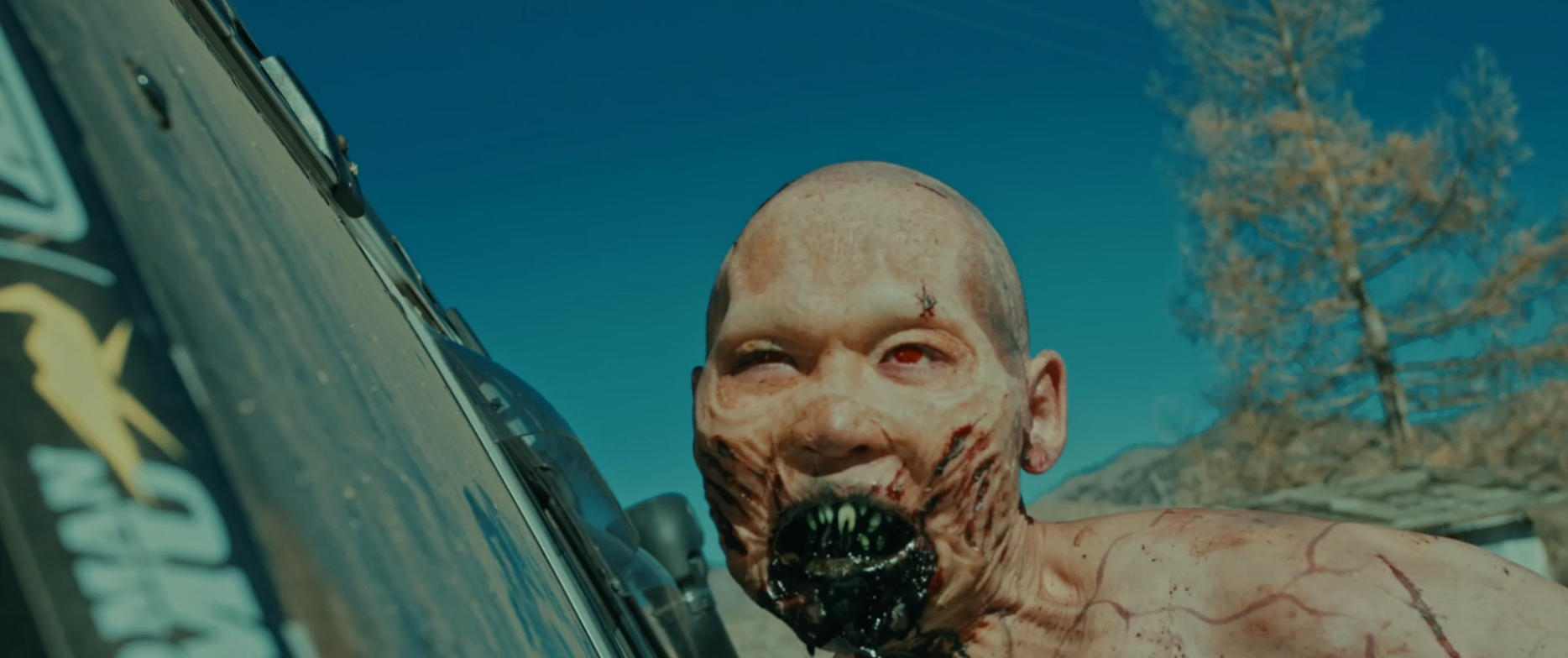 Ein blasser, verwundeter Zombie mit roten Augen blickt aus der Nähe auf eine Fahrzeugseite.