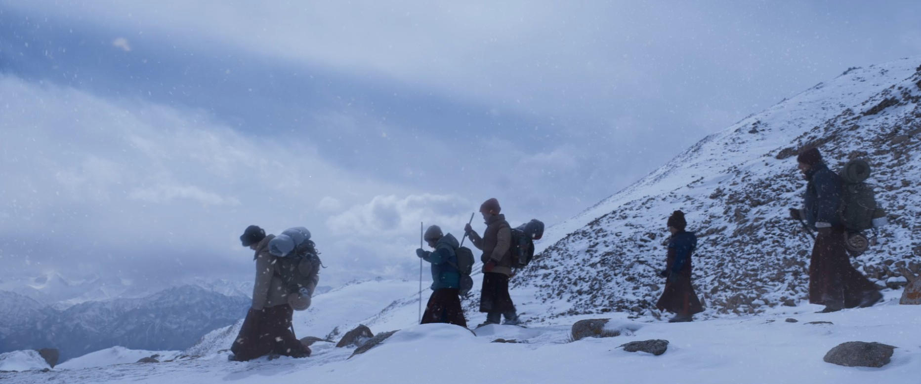 Fünf Wanderer in warmer Kleidung mit Rucksäcken gehen über einen schneebedeckten Hang.