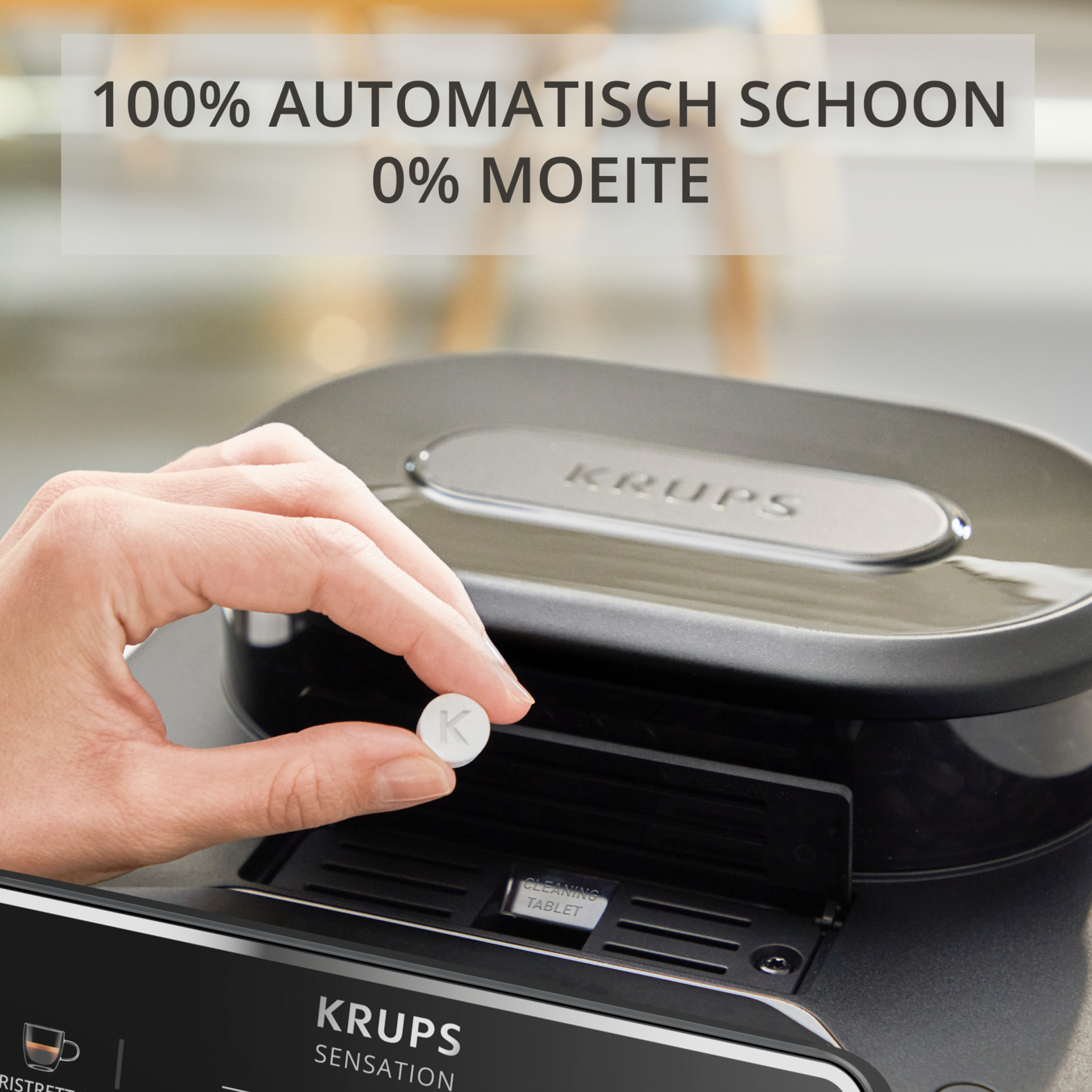 A hand holds a white cleaning tablet over a Krups coffee machine.