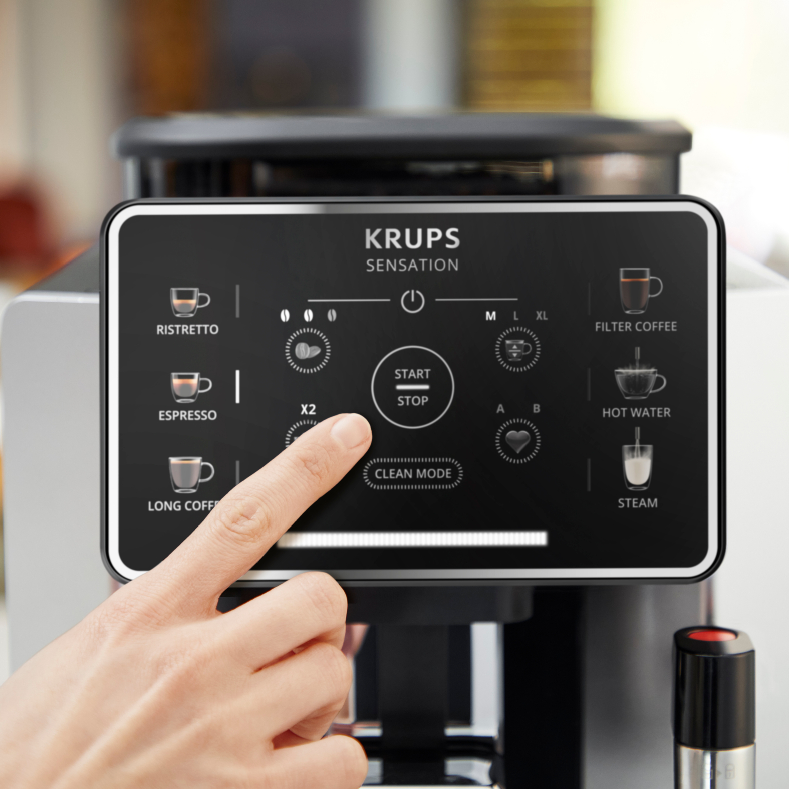A hand presses the start/stop button on a Krups coffee machine.
