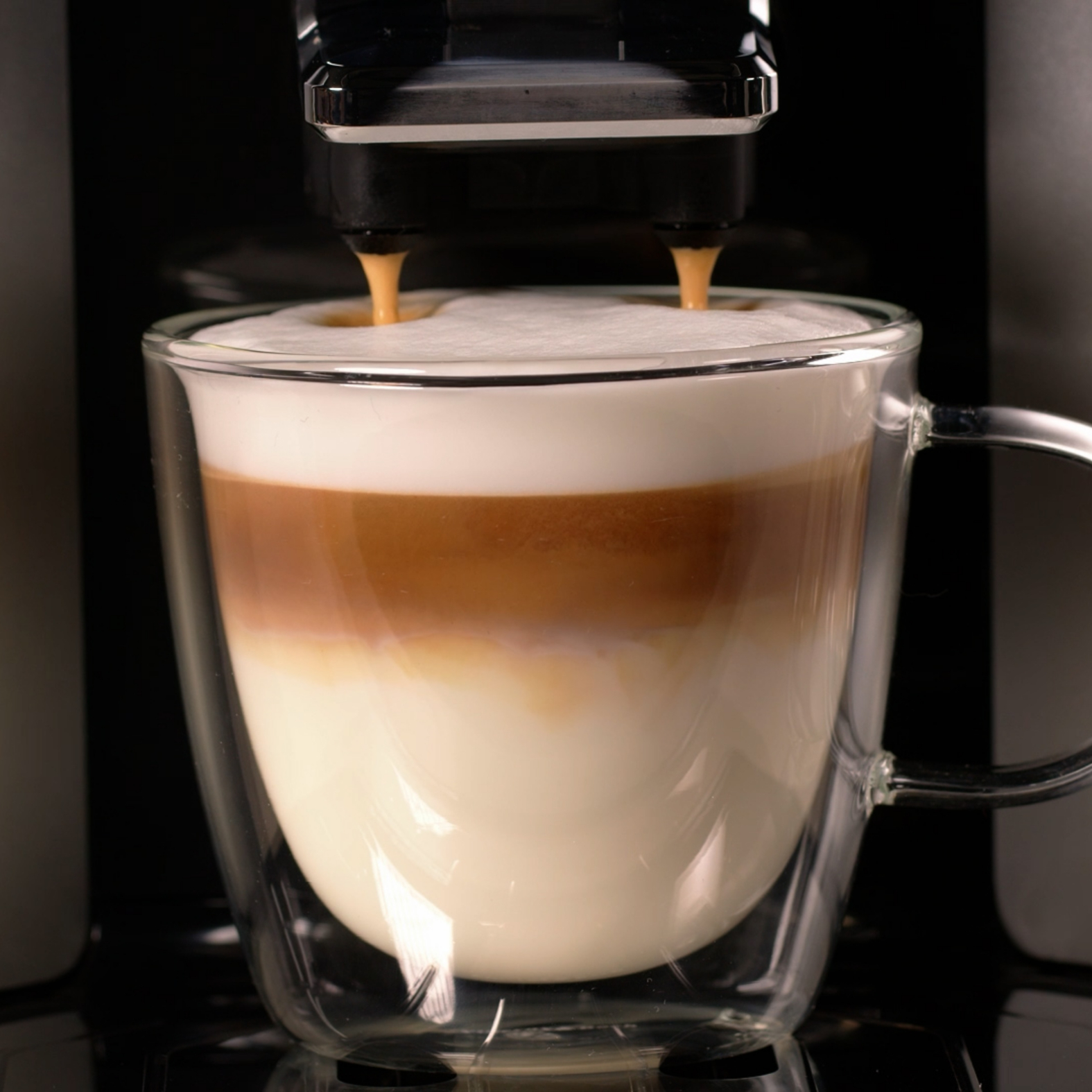 Coffee being poured into a glass with milk and foam.