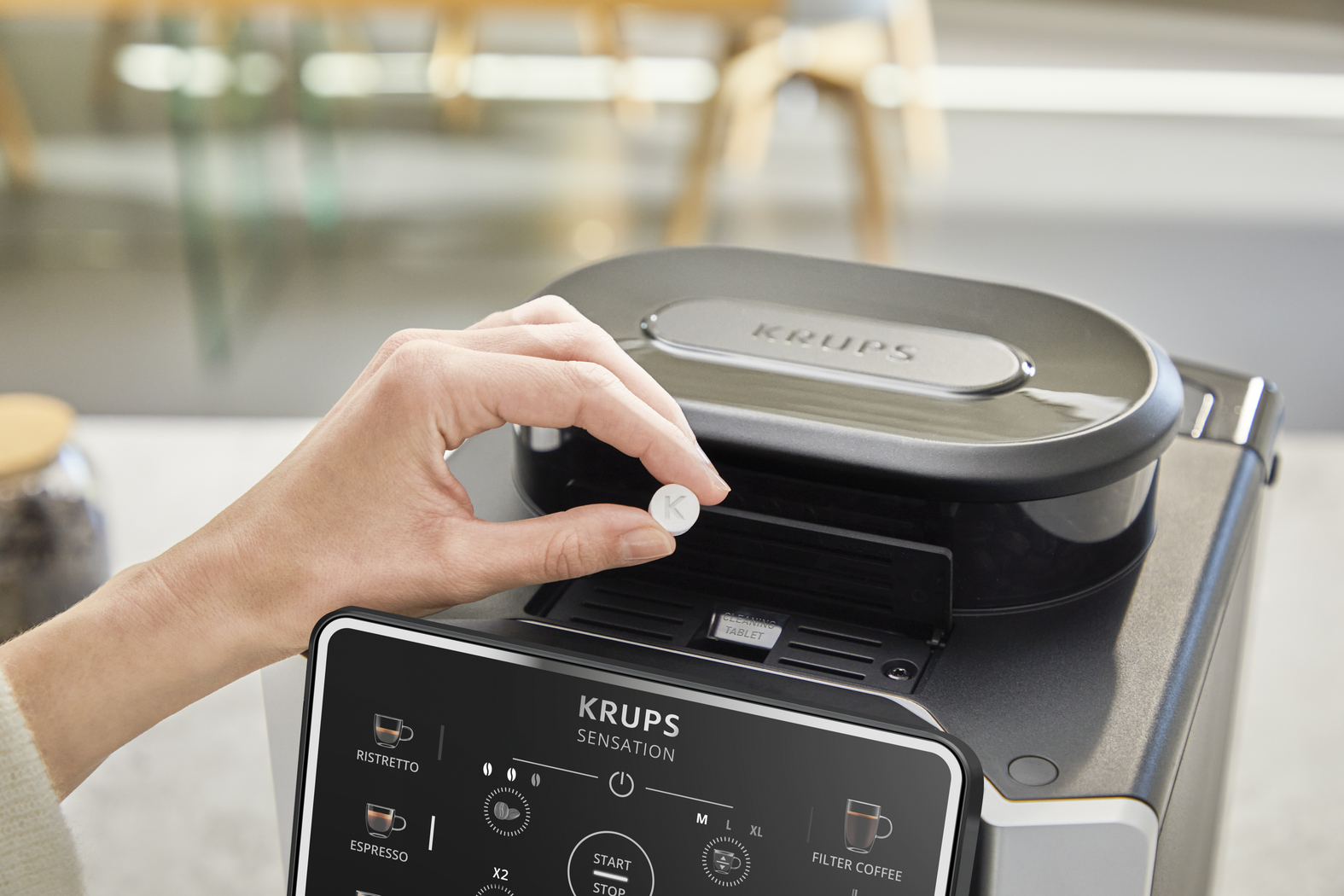 A hand places a white cleaning tablet into a coffee machine.