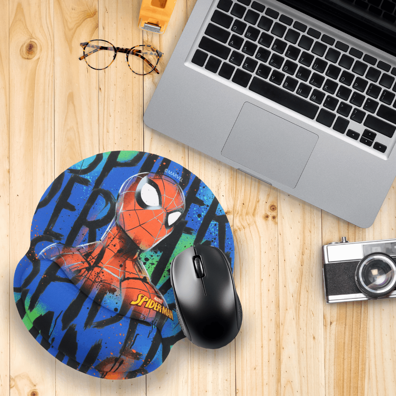 Alfombrilla de ratón de Spider-Man junto a portátil, ratón, gafas y cámara en escritorio.