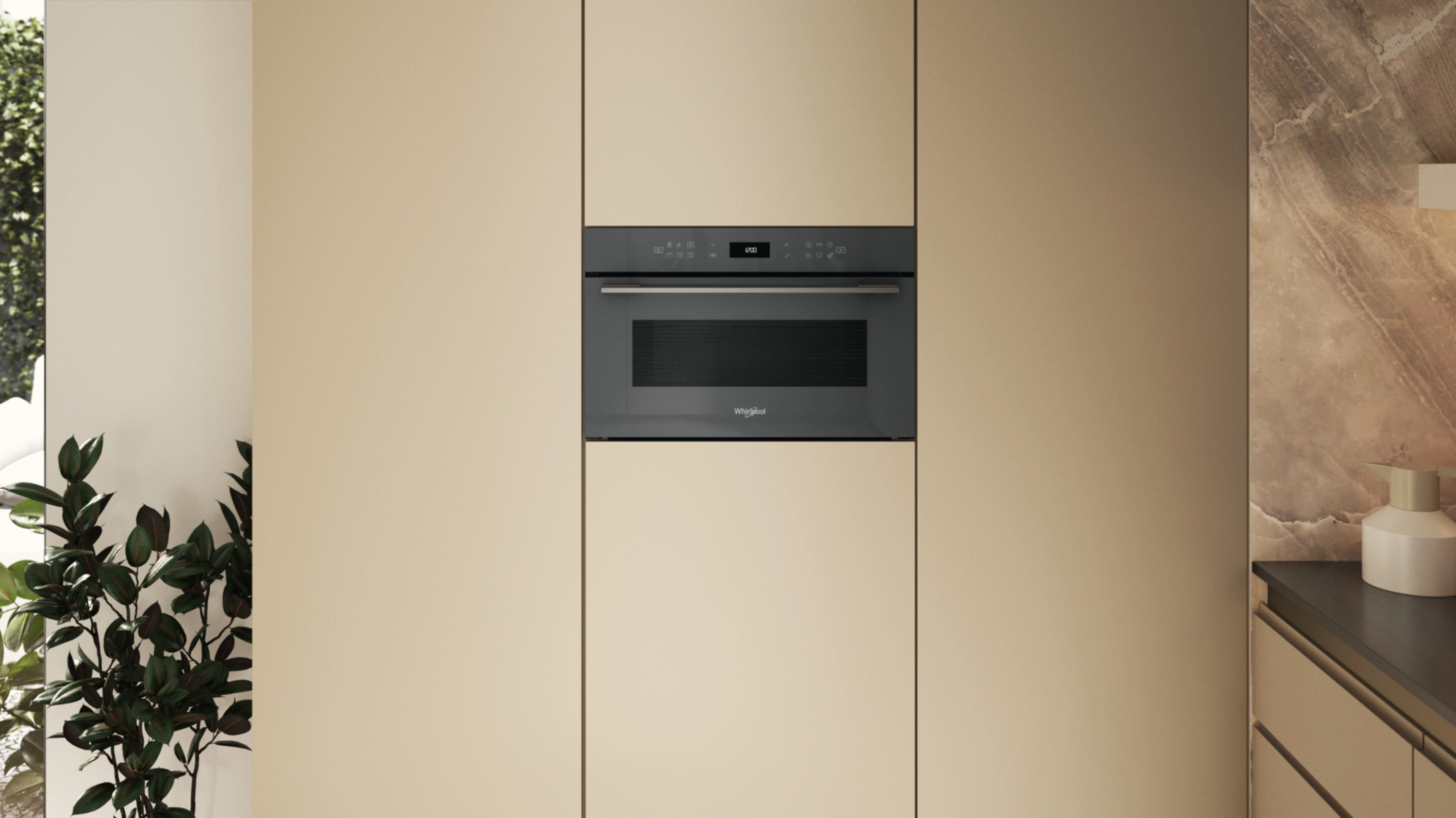 Nowoczesna kuchenka mikrofalowa w zabudowie w beżowych szafkach, obok okna z zielonymi roślinami.